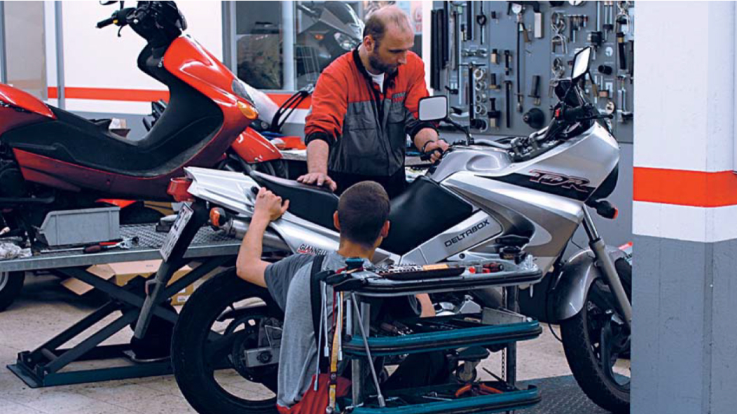 A picture of a workshop where two people are working on a motorbike.