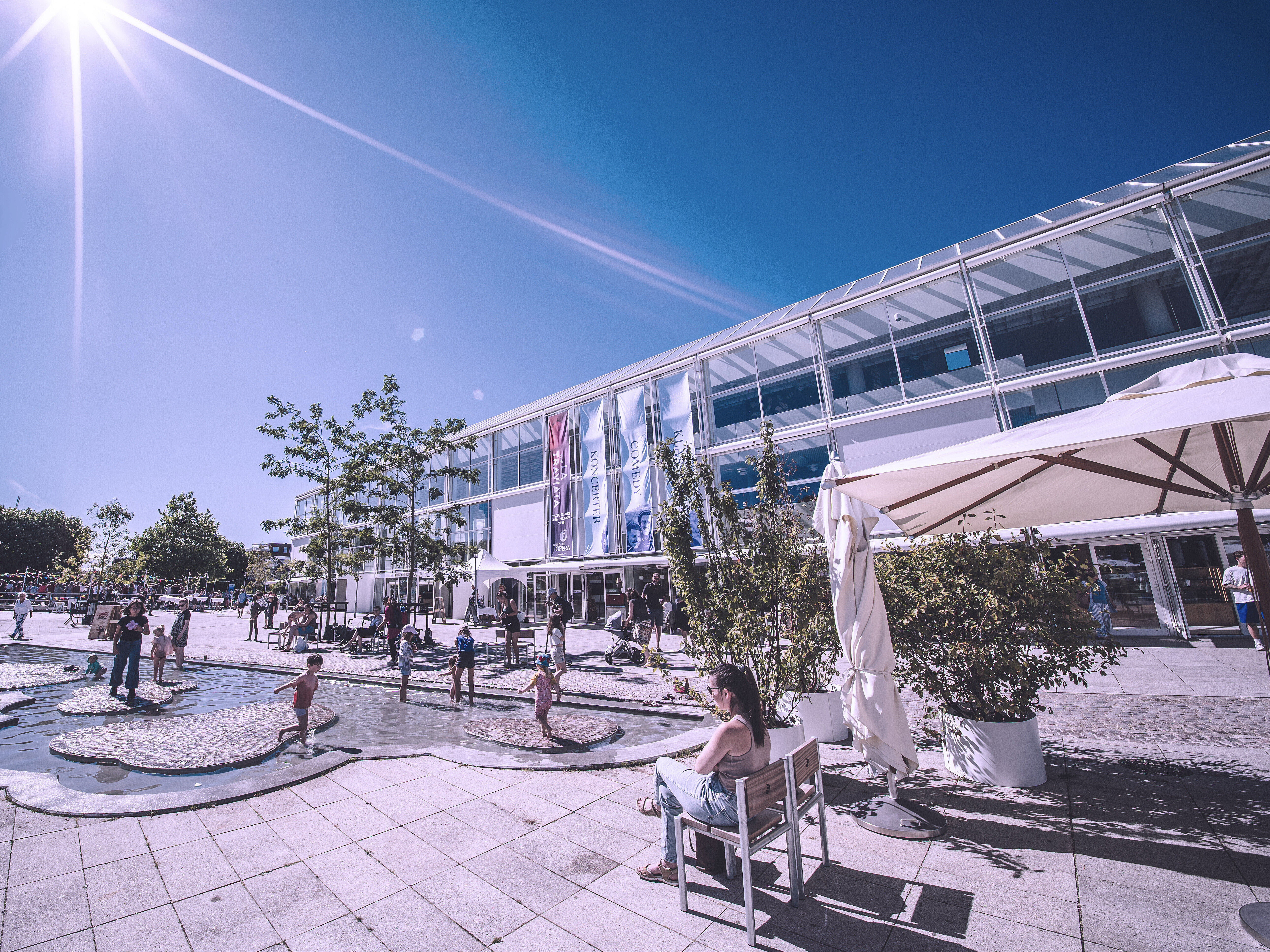 Forsiden af Musikhuset Aarhus i strålende solskin med mennesker foran indgangen