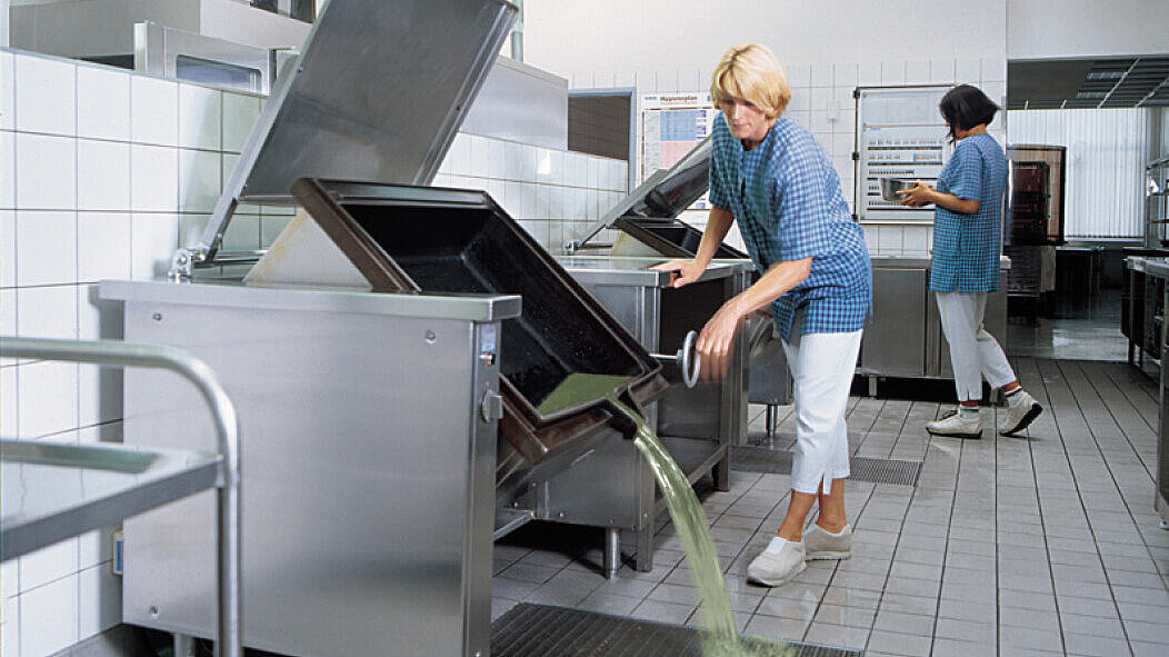 A large cooking pot is emptied into a floor tray in a commercial kitchen.